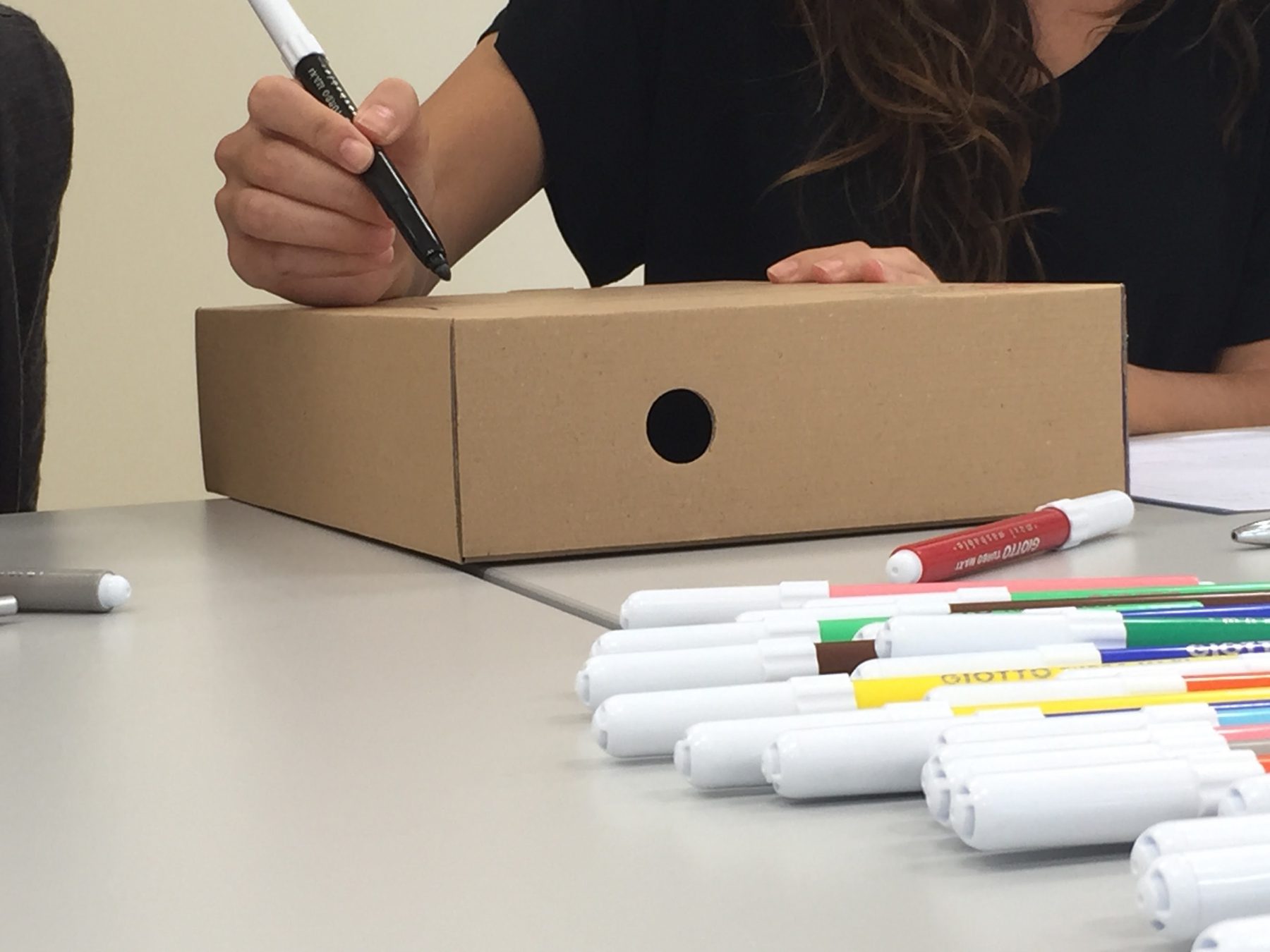 Chica escribiendo con rotulador sobre una caja de cartón para coceptualizar un proyecto 