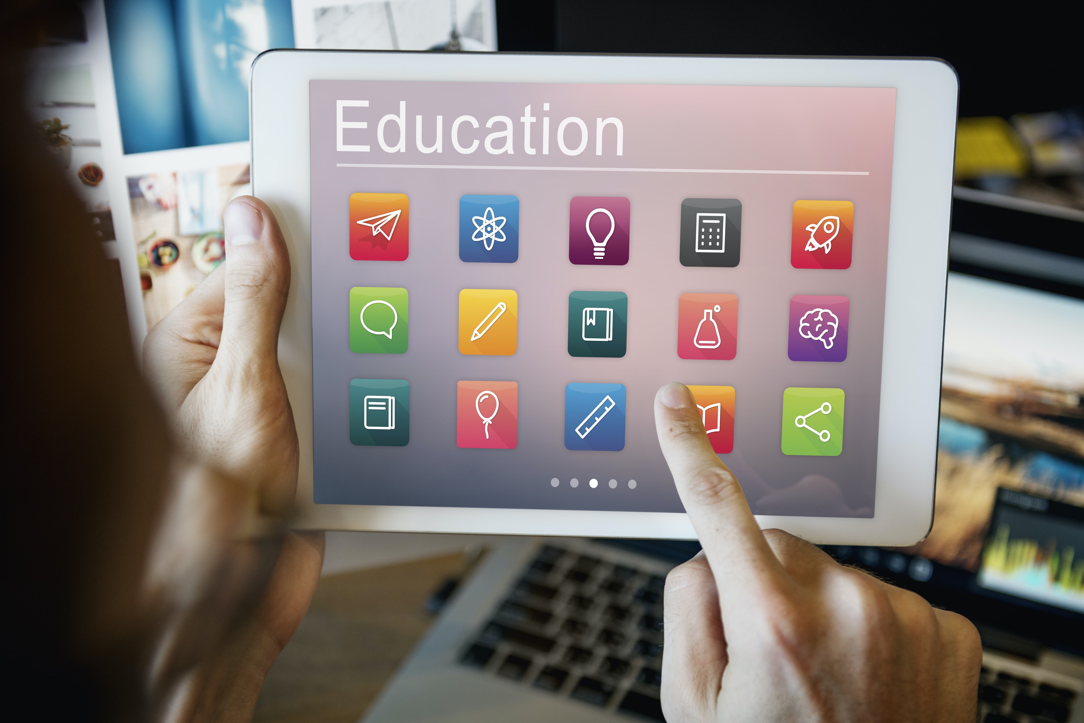 Fotografía de una Tablet sujetada por una persona con ambas manos en posición horizontal y tomada sobre el hombro de la persona. El fondo de la fotografía se muestra borroso y en la pantalla de la Tablet se muestra una galería de Apps con el título “Education” (Educación).