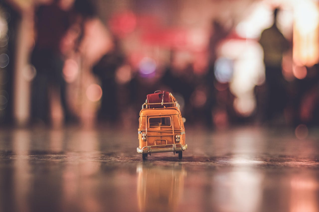 Imagen artística de un minibús de juguete amarillo sobre un piso reflejante con un fondo desenfocado de luces bokeh