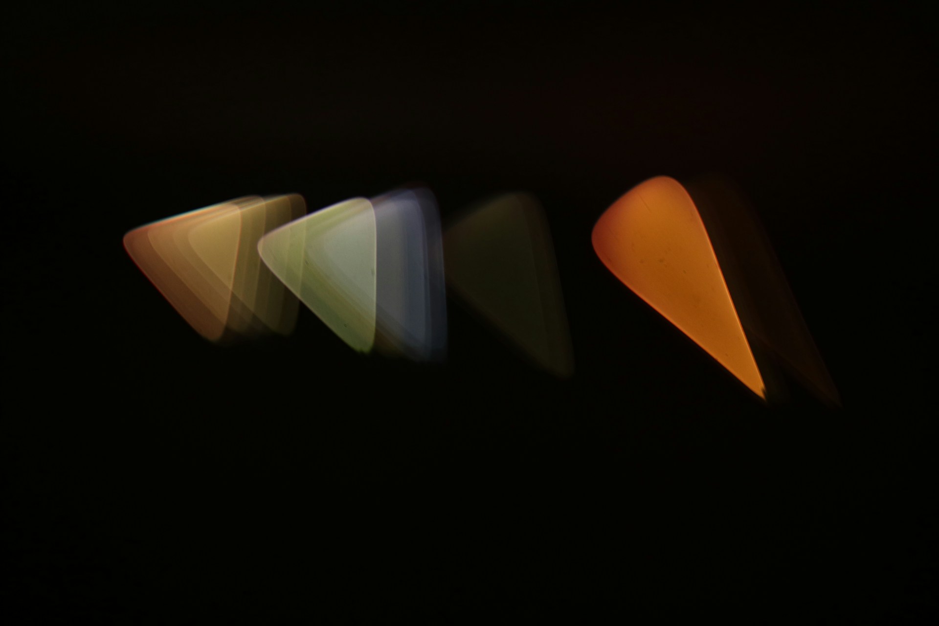 Imagen abstracta que muestra una secuencia de formas de púa de guitarra en perspectiva, con un efecto de desenfoque de movimiento que va del blanco al naranja, sobre un fondo oscuro, creando una sensación de movimiento y transición de colores.