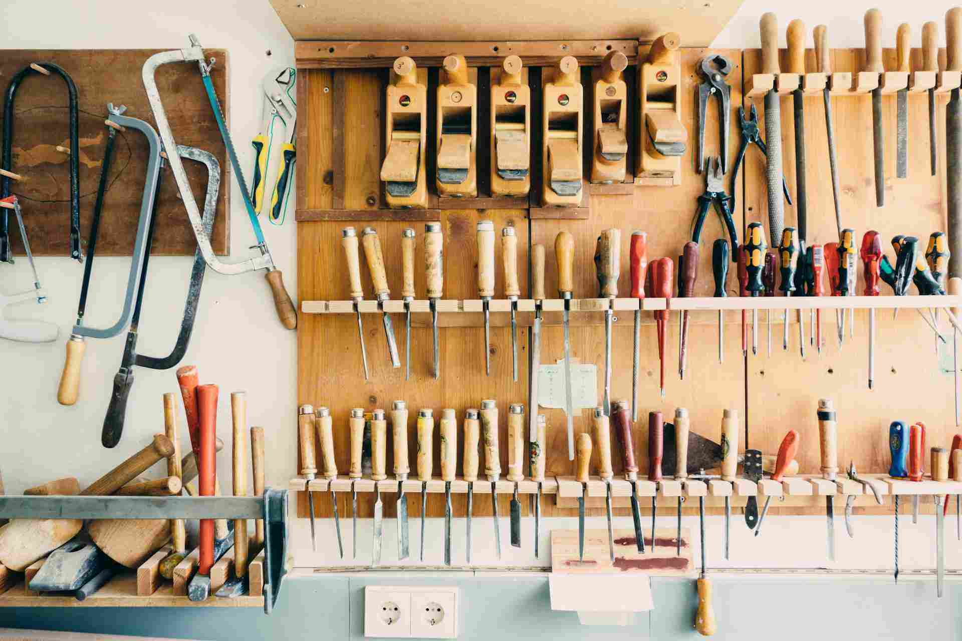 Tablero de herramientas montado en la pared de un taller, organizado meticulosamente con una variedad de herramientas manuales como sierras, cinceles, martillos y destornilladores, destacando un surtido completo para la carpintería.